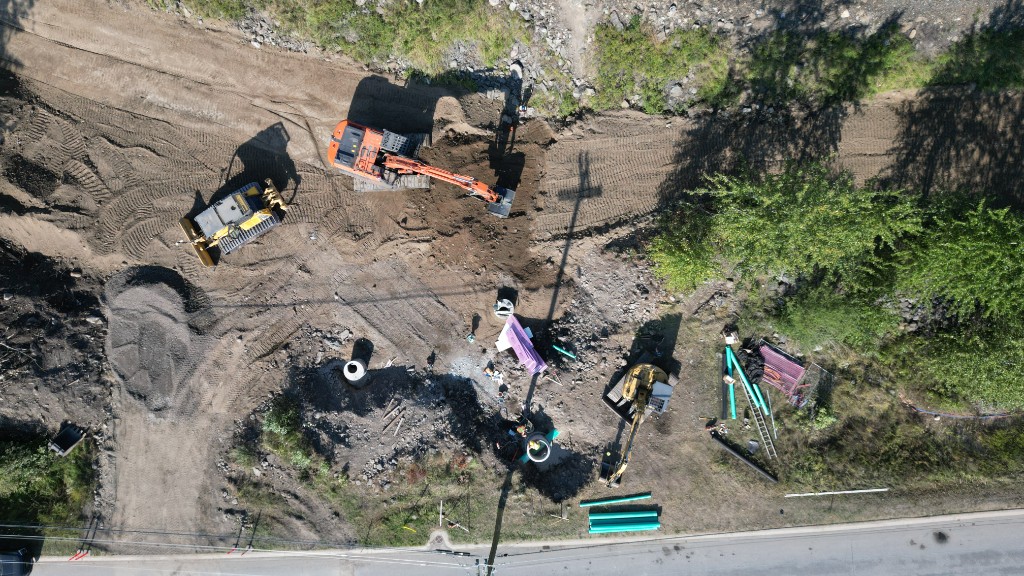 Construction workers at an open trench with excavation equipment compacting the trench floor